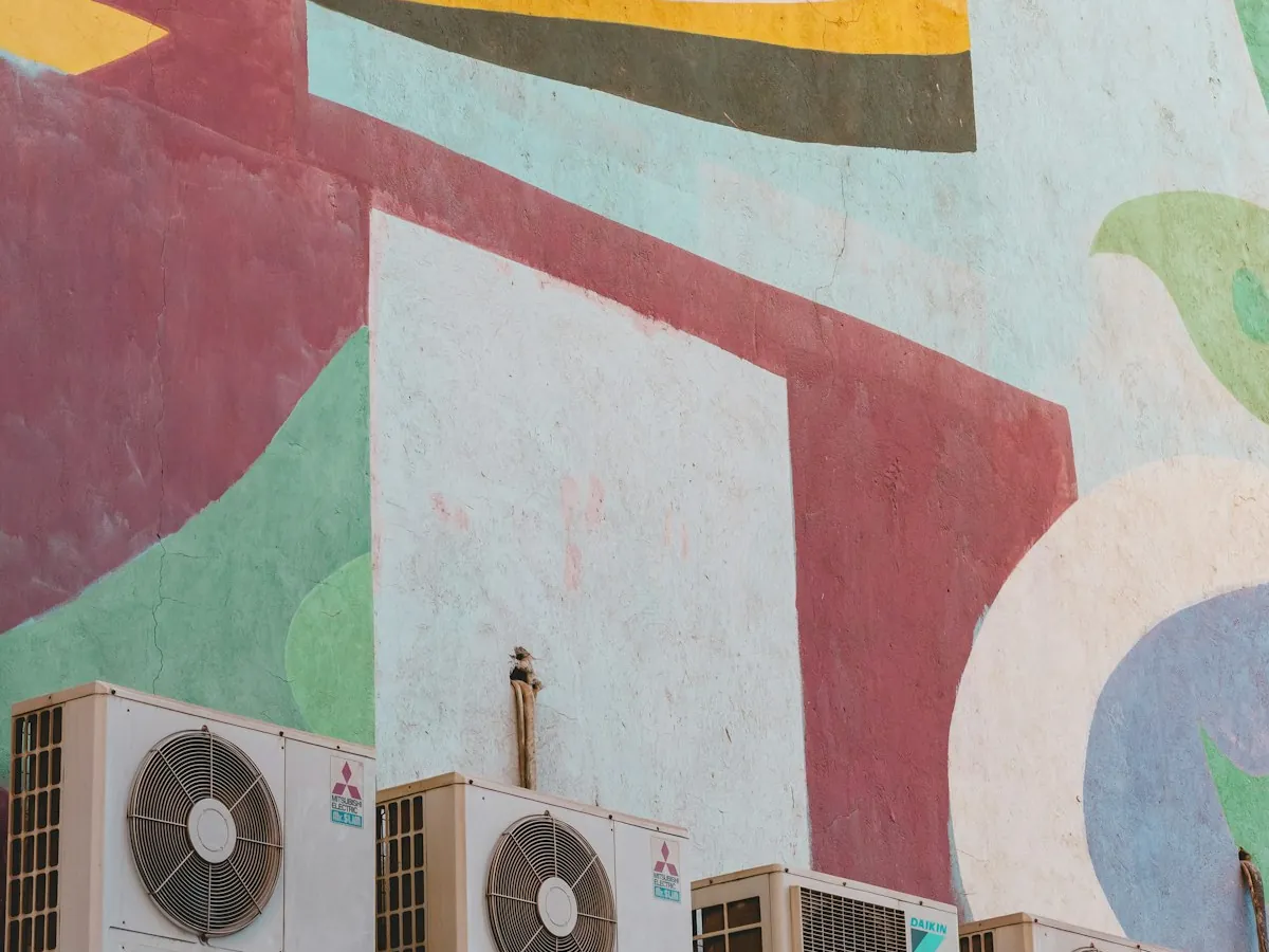 Row of outdoor AC condenser units against a painted mural wall