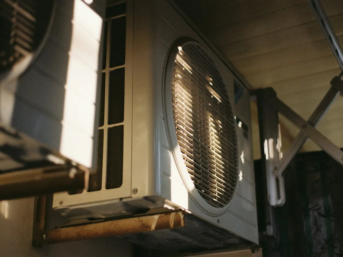 Wall-mounted outdoor AC condenser unit in warm sunlight