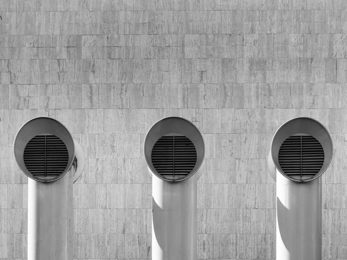 Three round ventilation duct outlets on a tiled building wall
