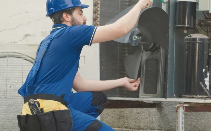 Technician in a hard hat servicing the fan of an outdoor AC unit