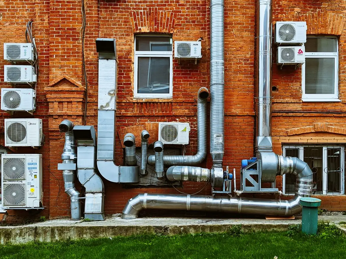 Brick building wall with split AC units, metal ductwork and an extraction fan